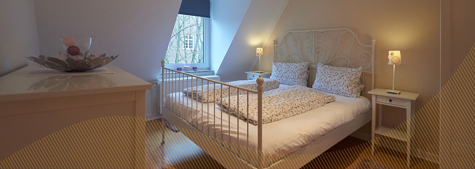 Schlafzimmer mit Dachschräge und einem Doppelbett aus Metall, helle Bettwäsche mit Blumen